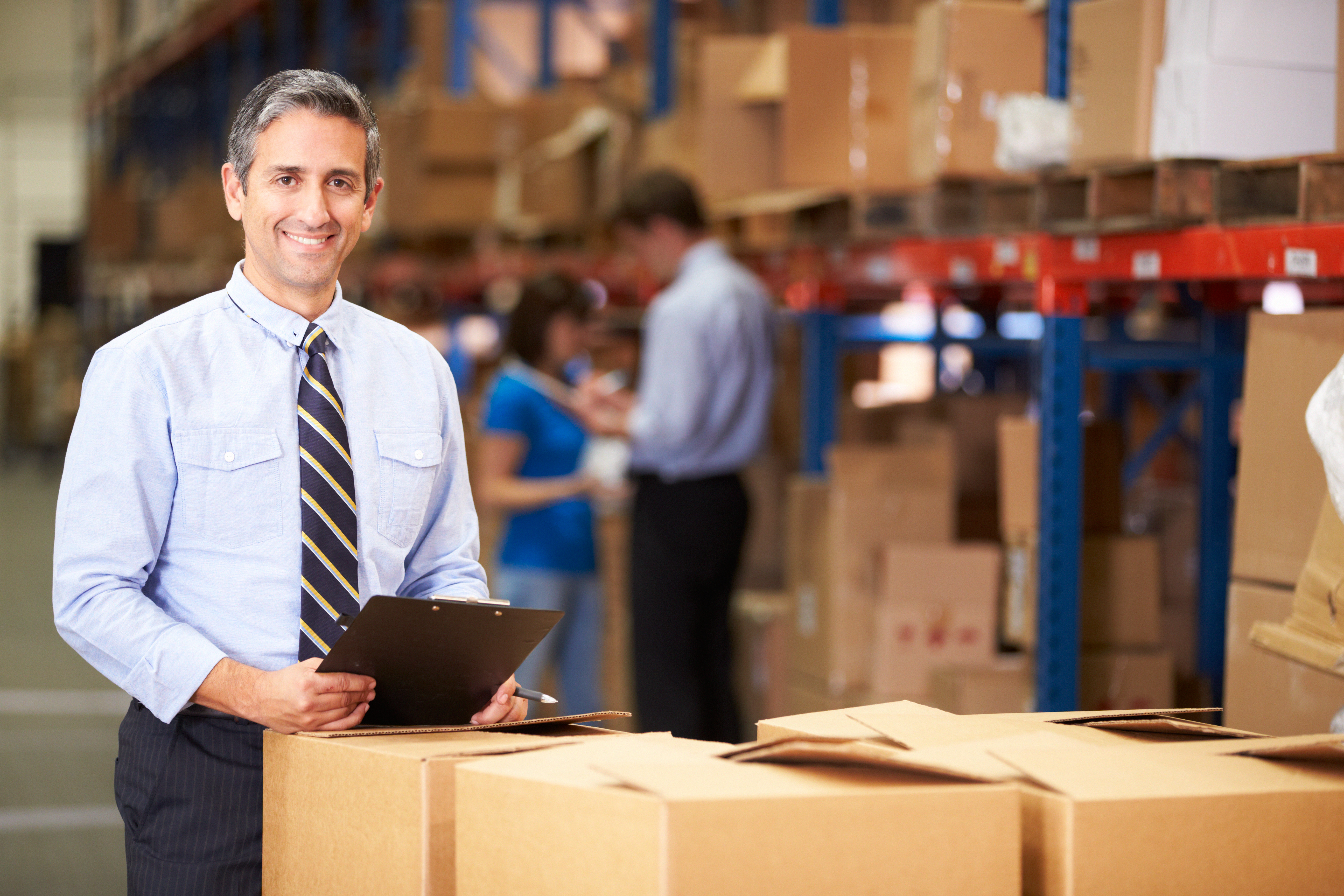 A man wearing a suit holding a clipboard in a warehouse.