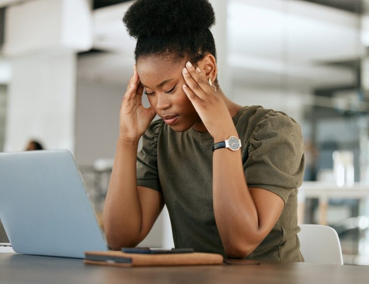 Woman sitting in front of a laptop rubbing her temples. 