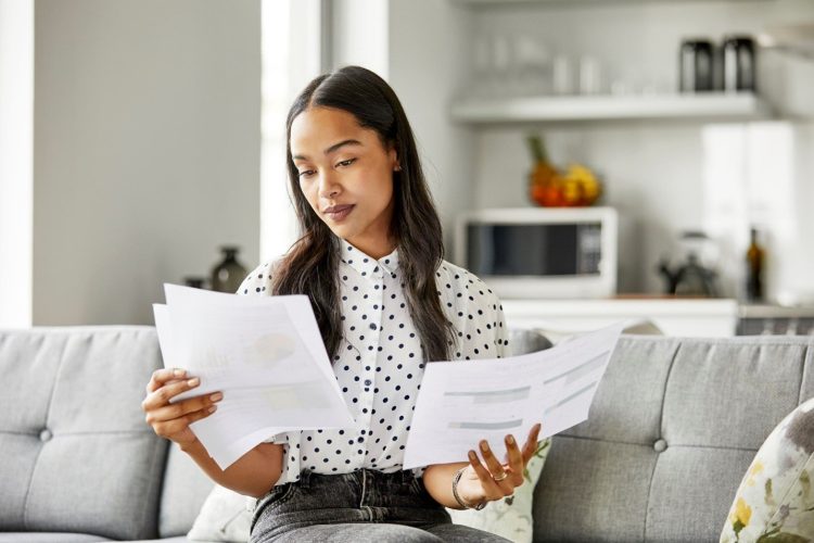 A woman looking at sheets of paper in both of her hands. 