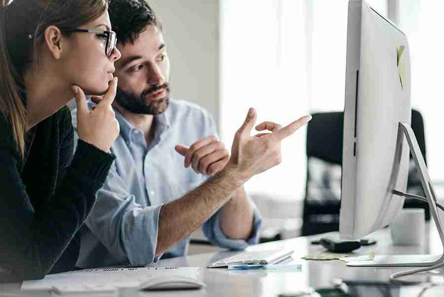 A man and a woman looking at a computer monitor. 