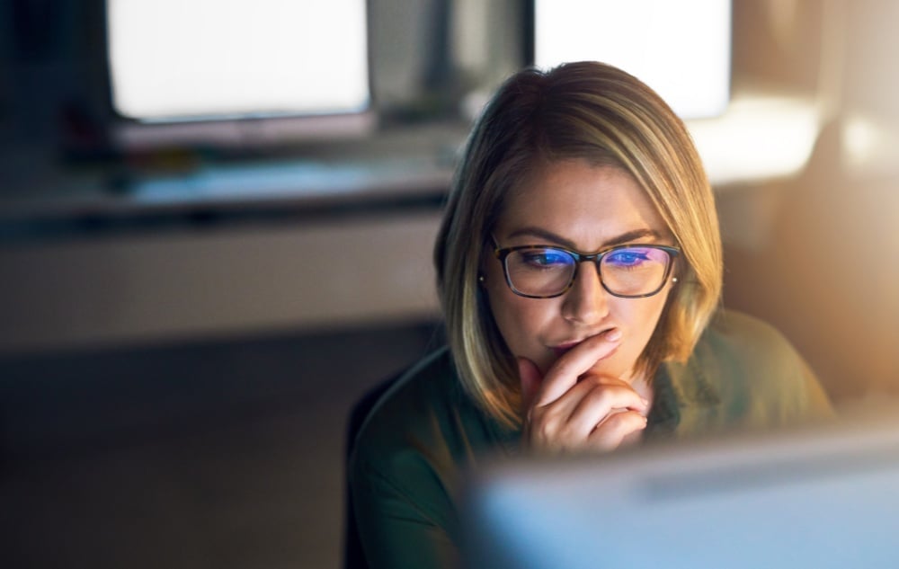 woman with a contemplative look on her face looking at a computer monitor.