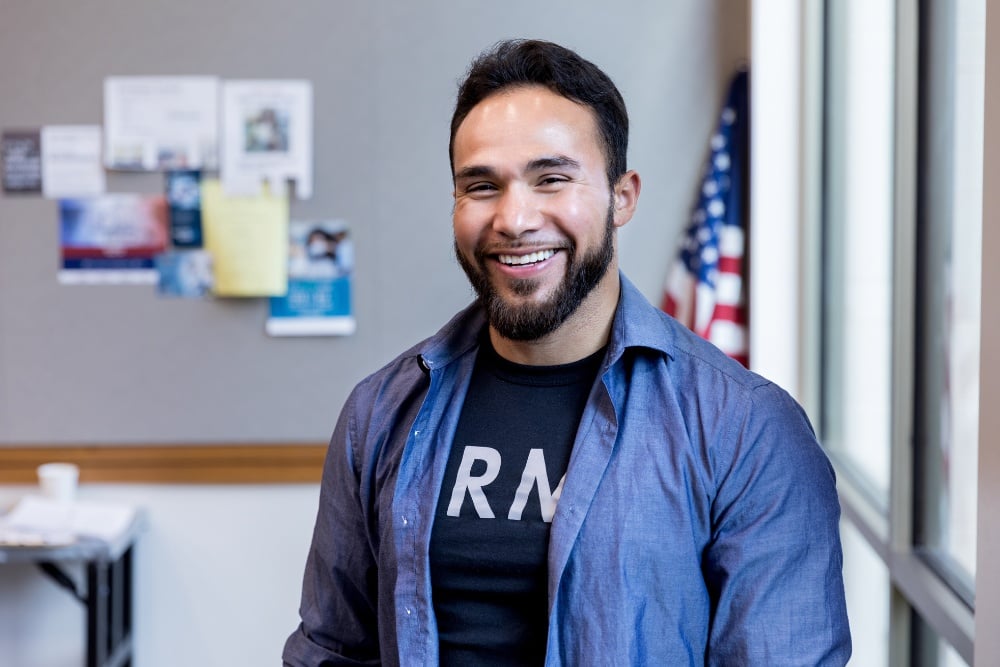 A veteran wearing a black army shirt smiling at the camera. 