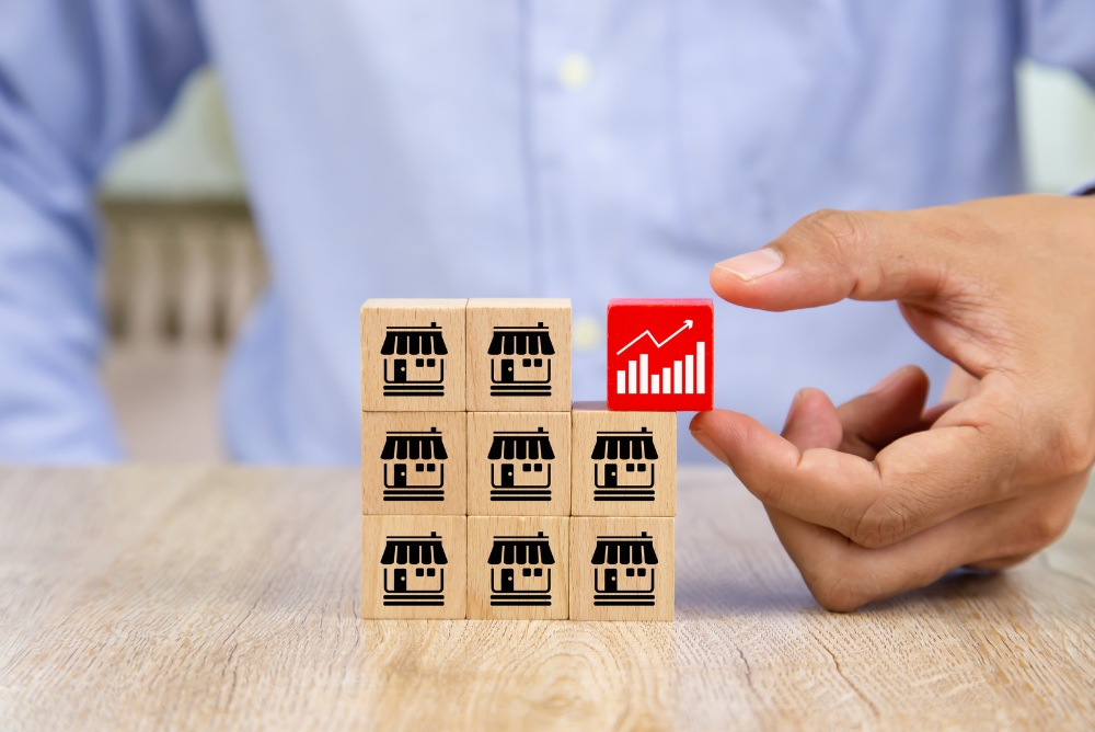 Wooden blocks with home symbols stacked 3 by 3 with the top right being a red wooden block with a stocks symbol.  